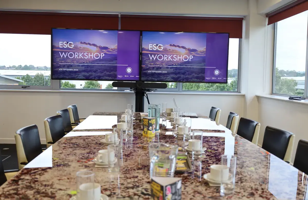 A meeting room with a large table and two tv screens. 