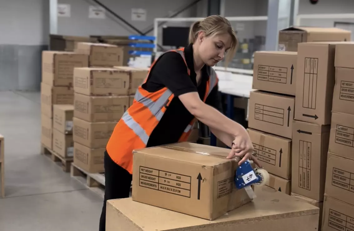 Female operative wearing a high vis vest, taping a box ready for dispatch.