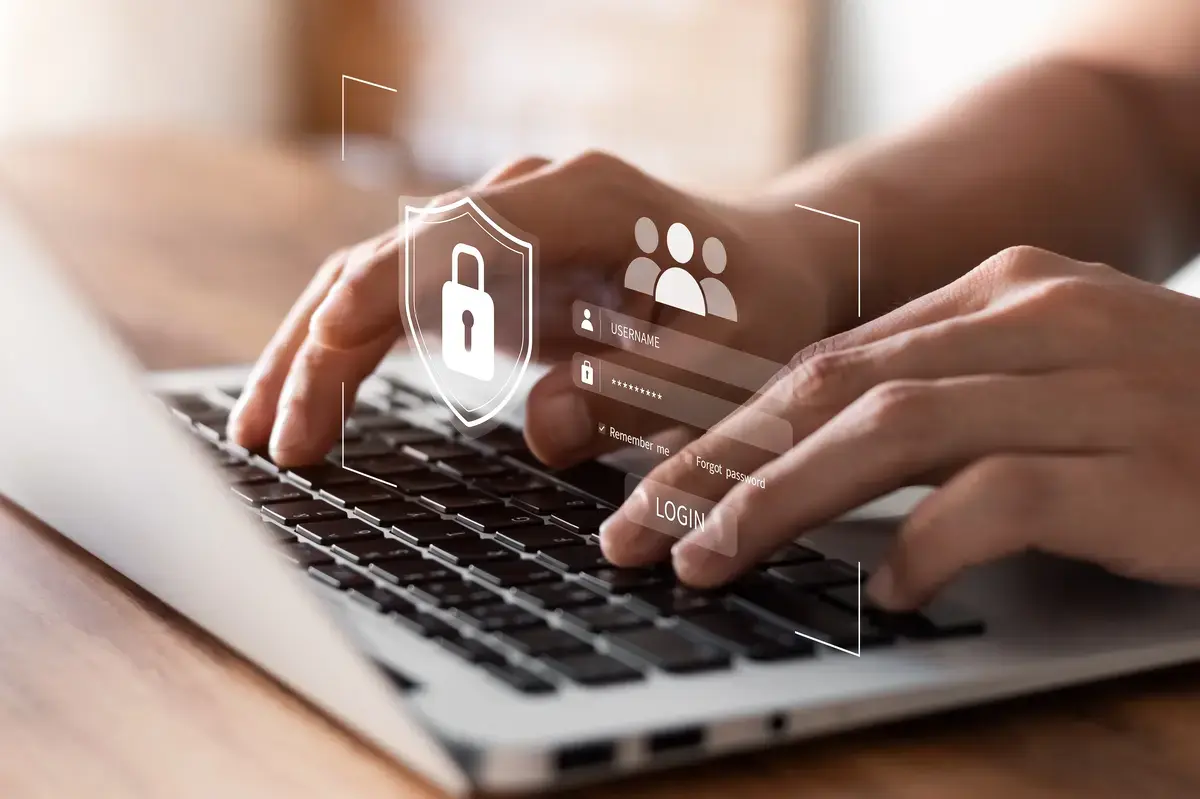 A person typing on a laptop, with a prominent security icon displayed on the screen, emphasizing digital safety.