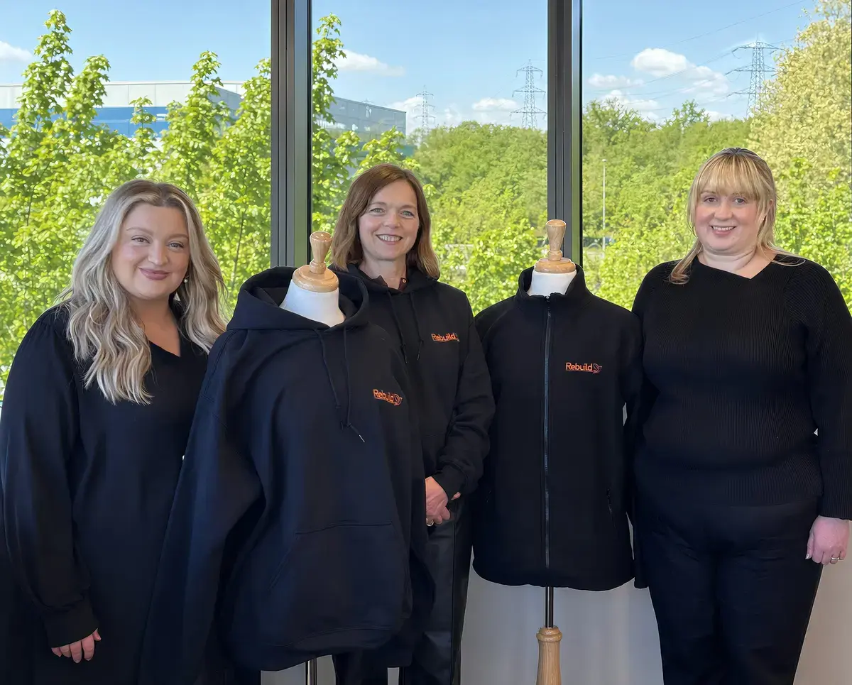 Three women are stood together alongside two mannequins wearing black fleeces. 
