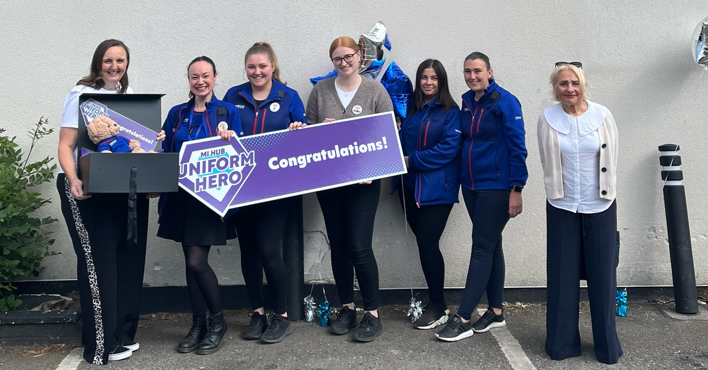A group of people stood together holding a congratulations sign and balloons. 