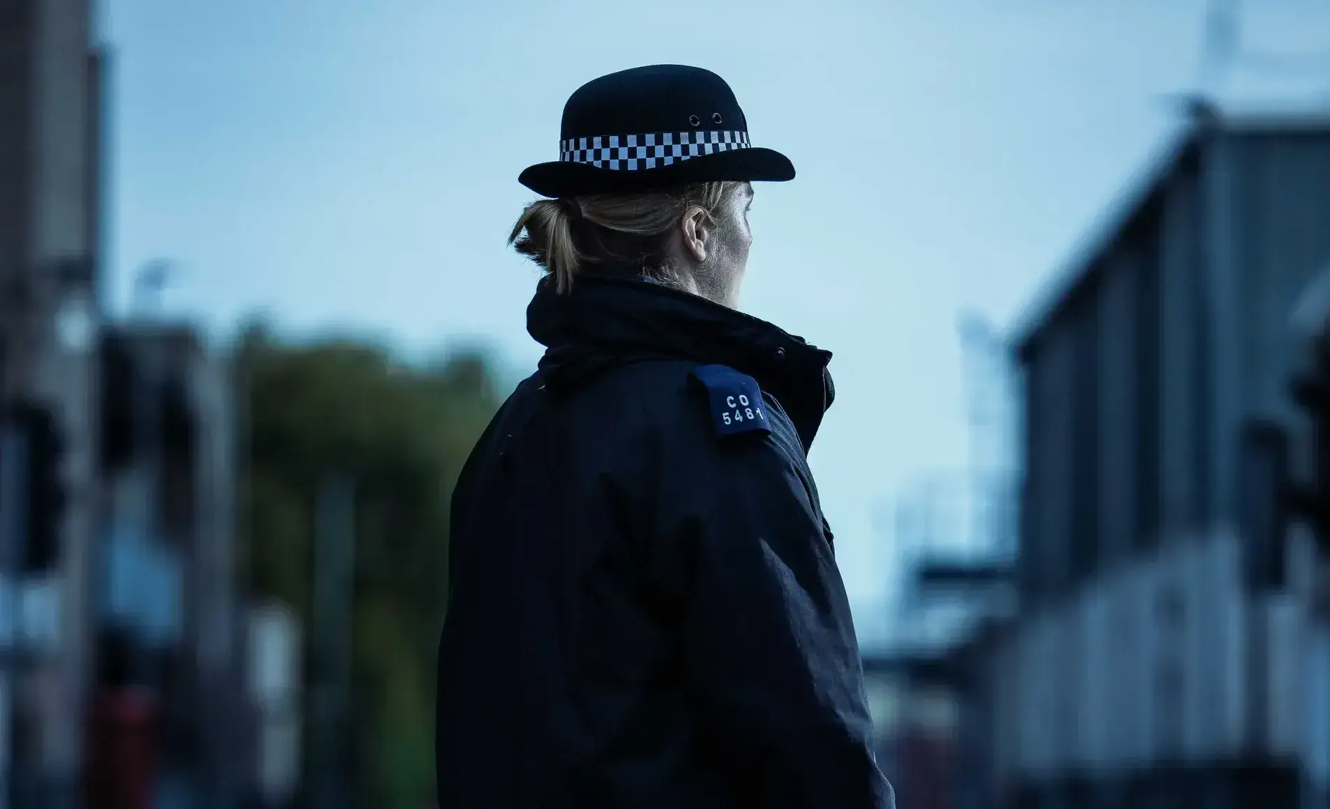 The back of a police officer stood in the street wearing uniform.